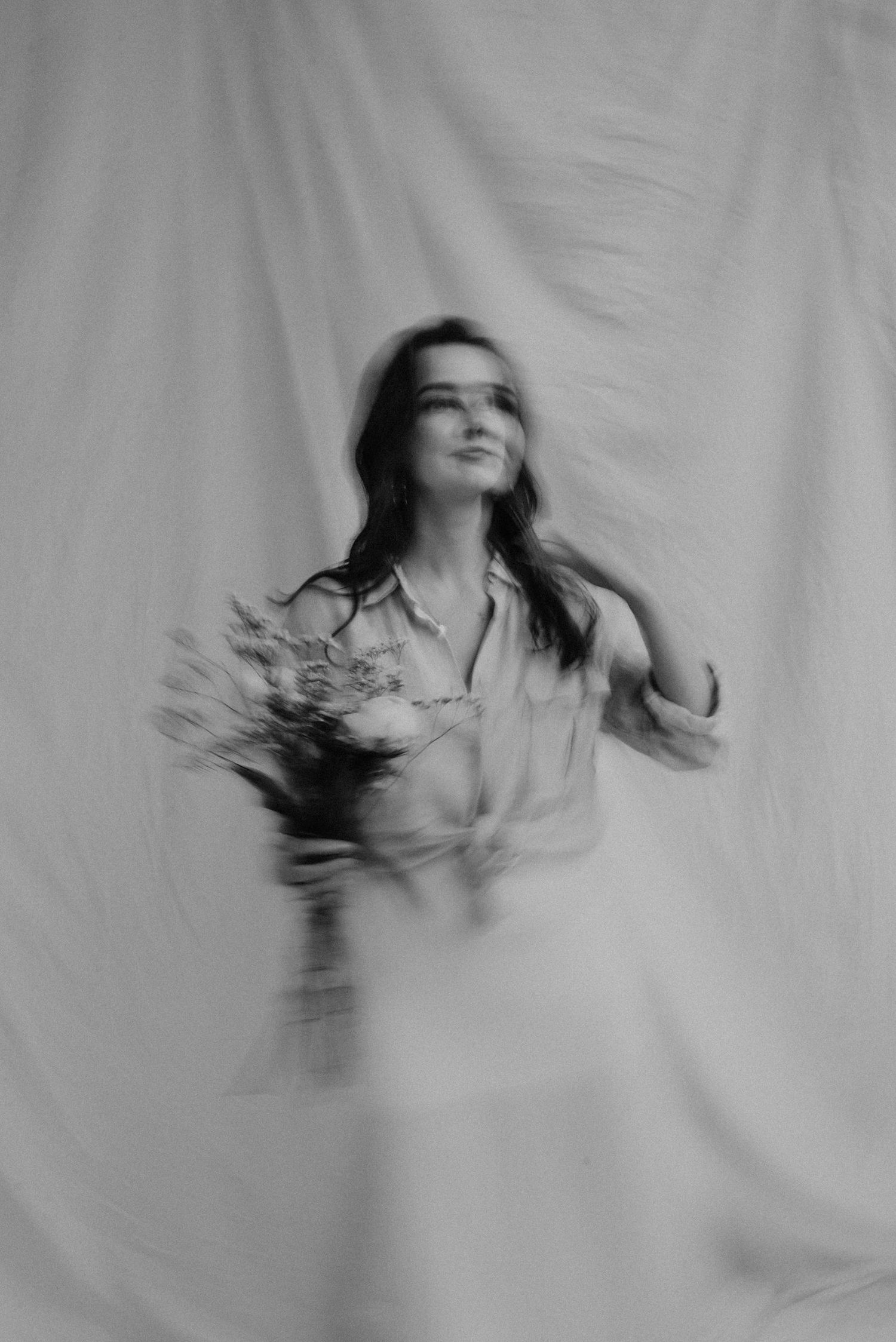 Artistic motion blur portrait in soft lighting against white fabric backdrop.