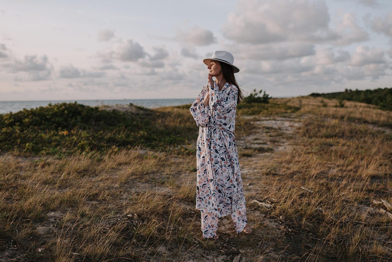 A floral dress flows in the breeze against a dramatic coastal landscape.