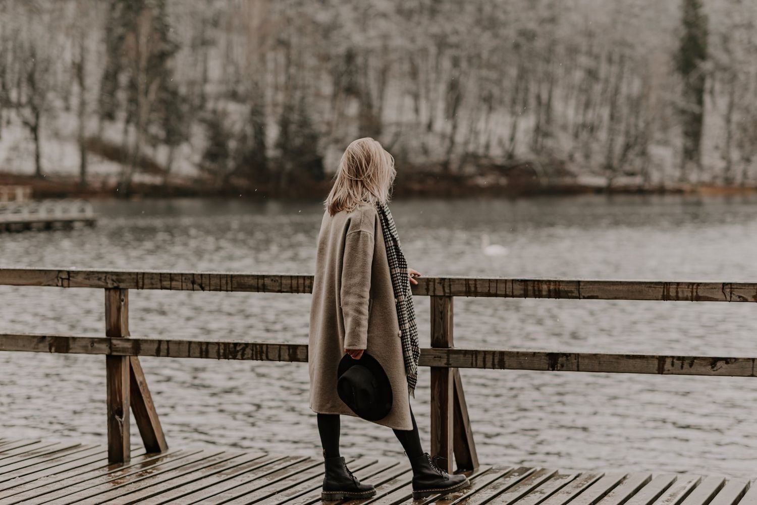 Figure walks along a wooden boardwalk in winter wearing a long coat.