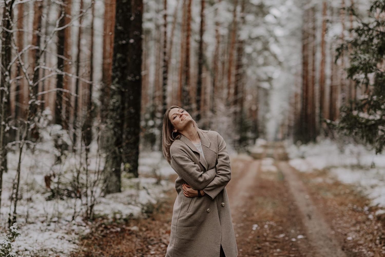 Snowy forest path with tall pine trees and a person walking in winter attire.