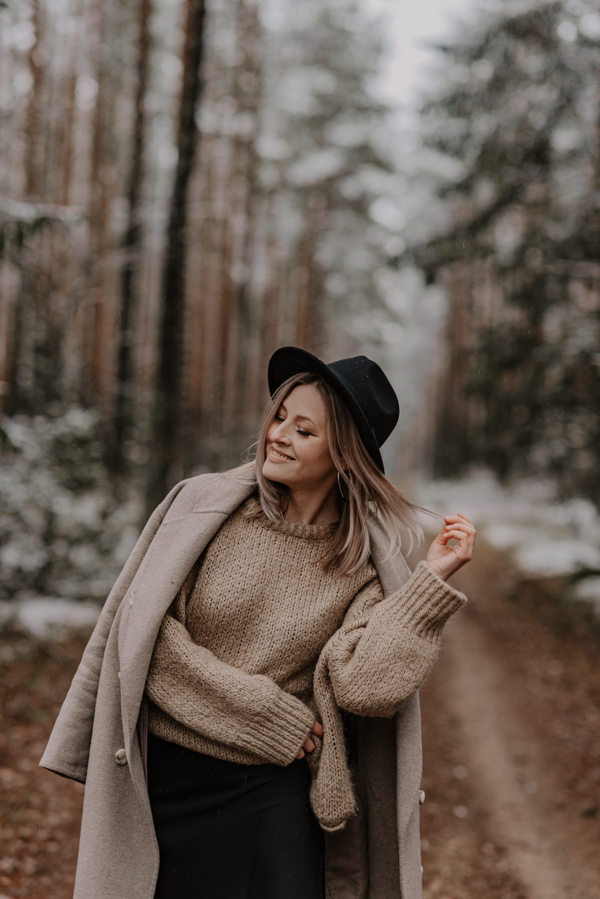 Winter fashion photography in a snowy forest featuring cozy sweater and hat styling.