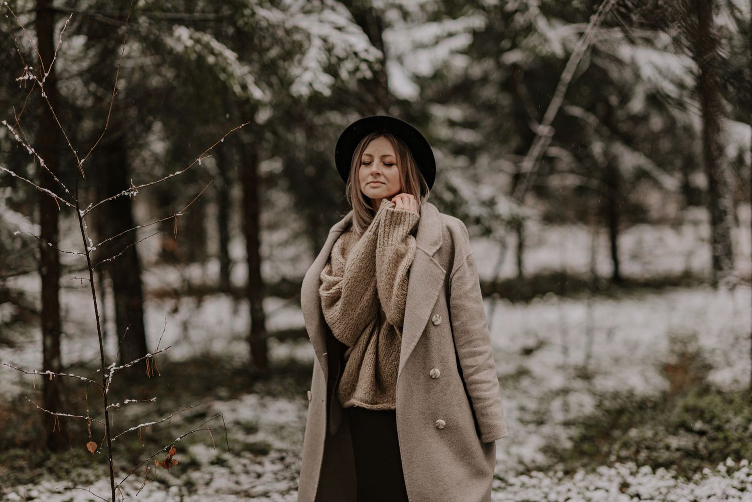 Moody winter portrait session among snow-covered pine trees in a forest.