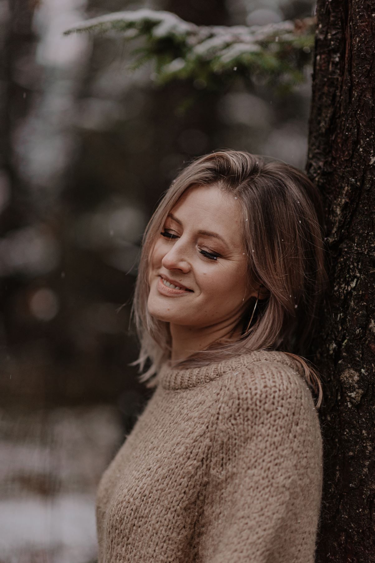A person in a knit sweater enjoys a peaceful moment leaning against a tree trunk in a forest setting.