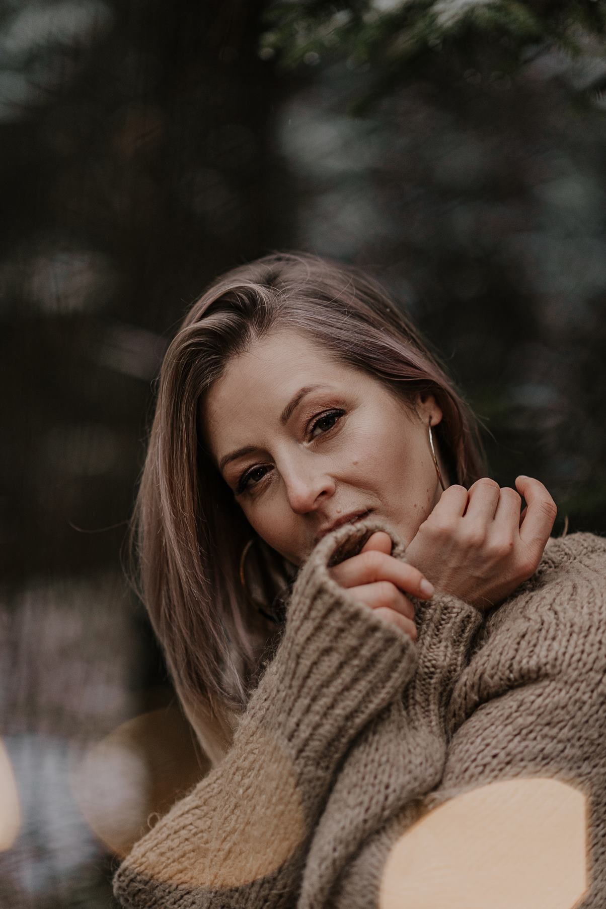 Someone wearing a cozy turtleneck sweater poses playfully against a dark forest backdrop.