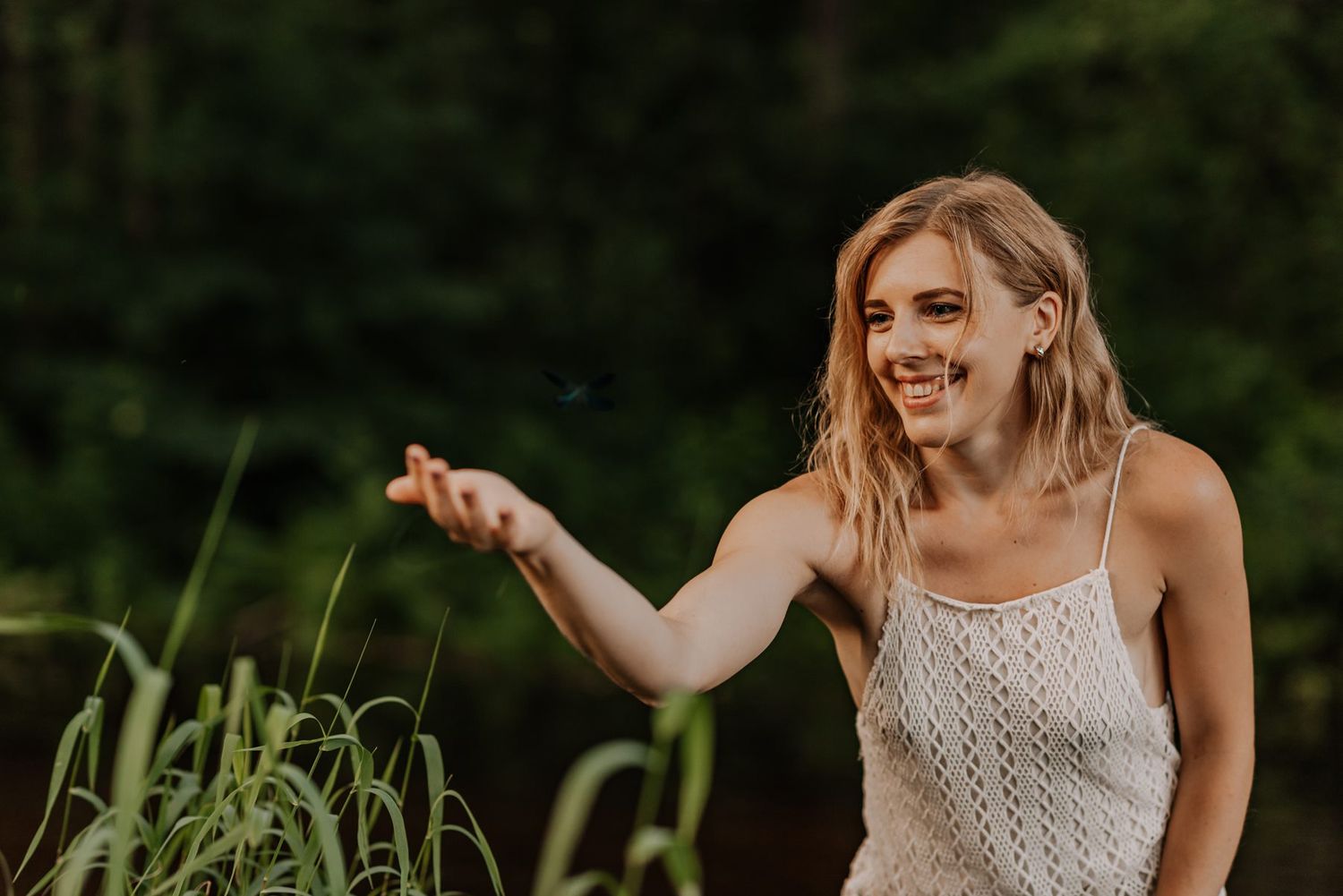 A woman in a white summer dress gestures playfully in a forest setting.
