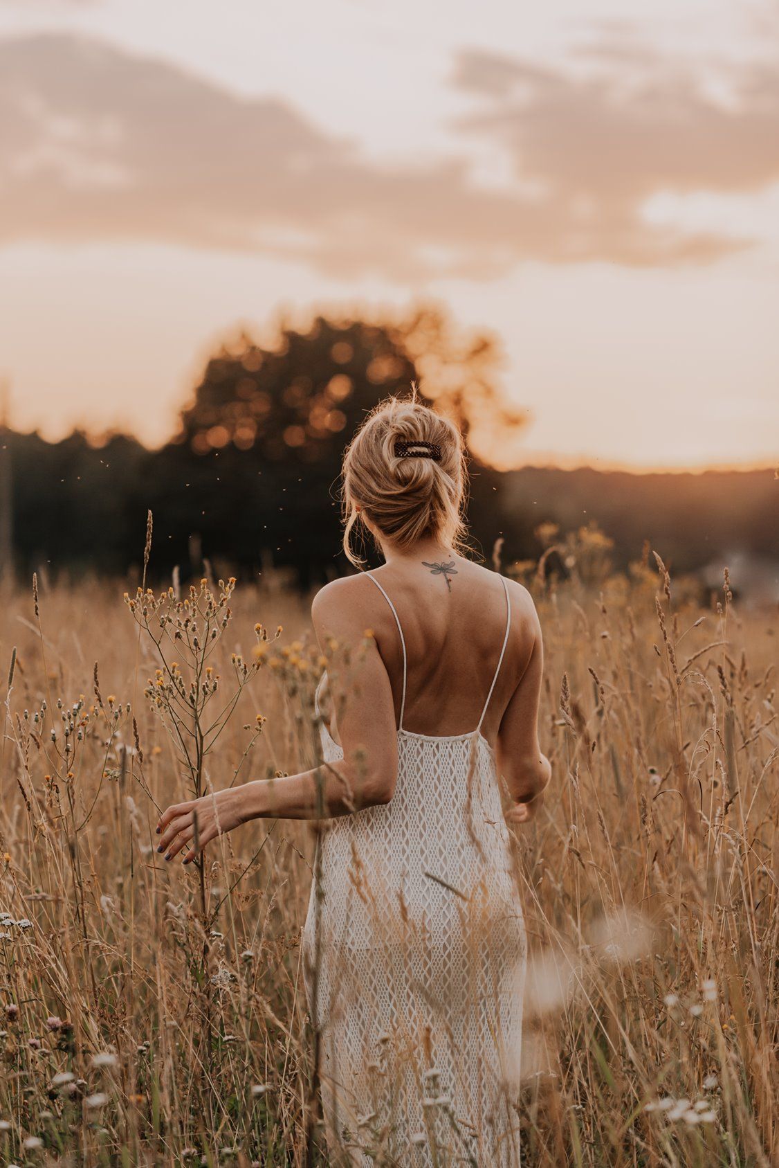 A woman in a white dress stands in a golden wheat field at sunset.