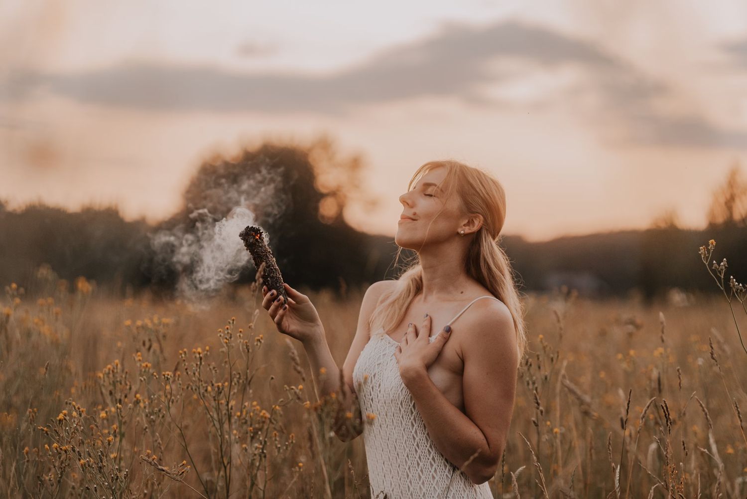 Figure in white dress stands in tall grass during golden hour.