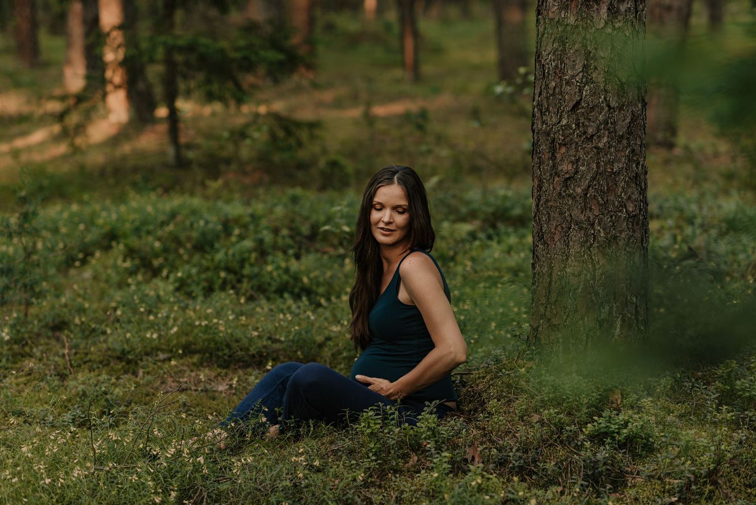 Woman reclining on forest ground surrounded by pine trees.