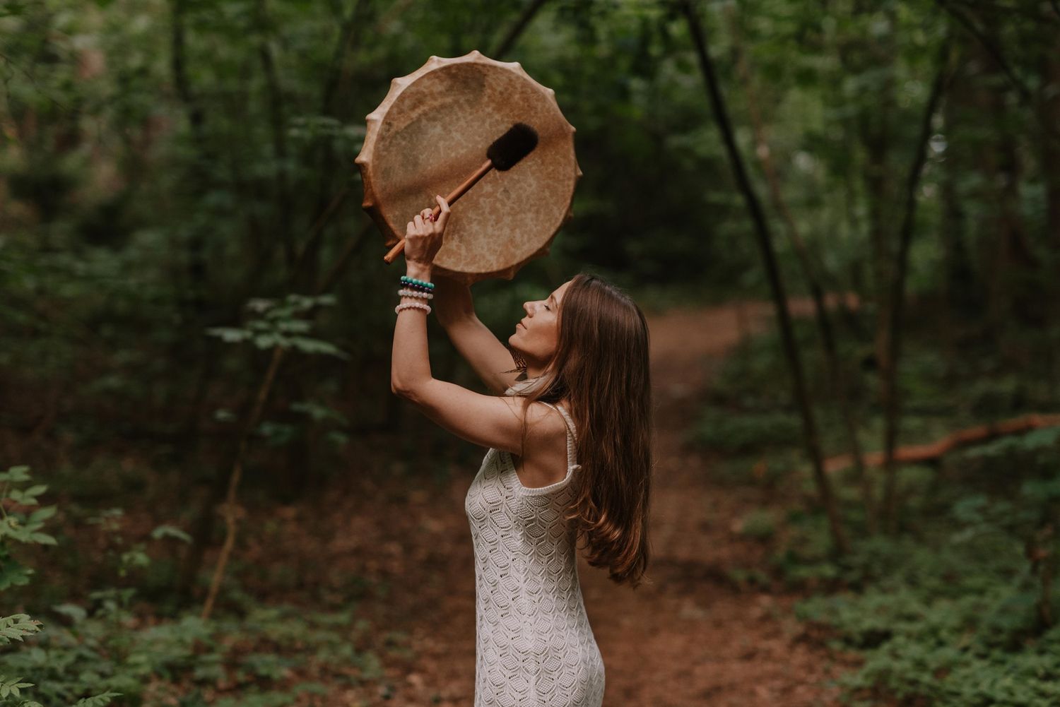 A person in summer attire dances joyfully among trees in a sunlit forest clearing.