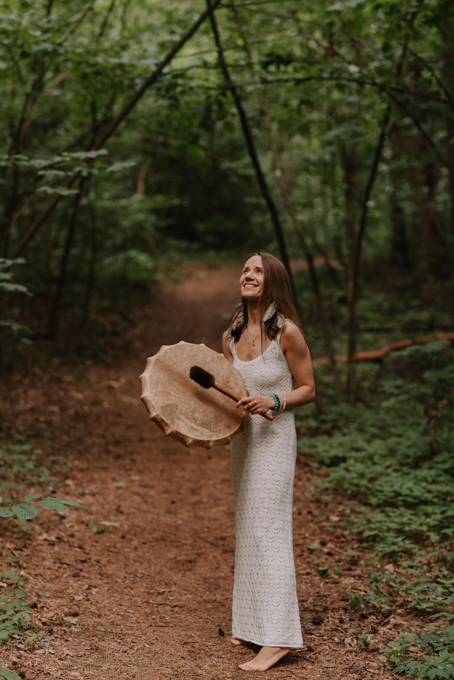 A woman in a white dress dances joyfully on a forest path surrounded by lush greenery and trees.