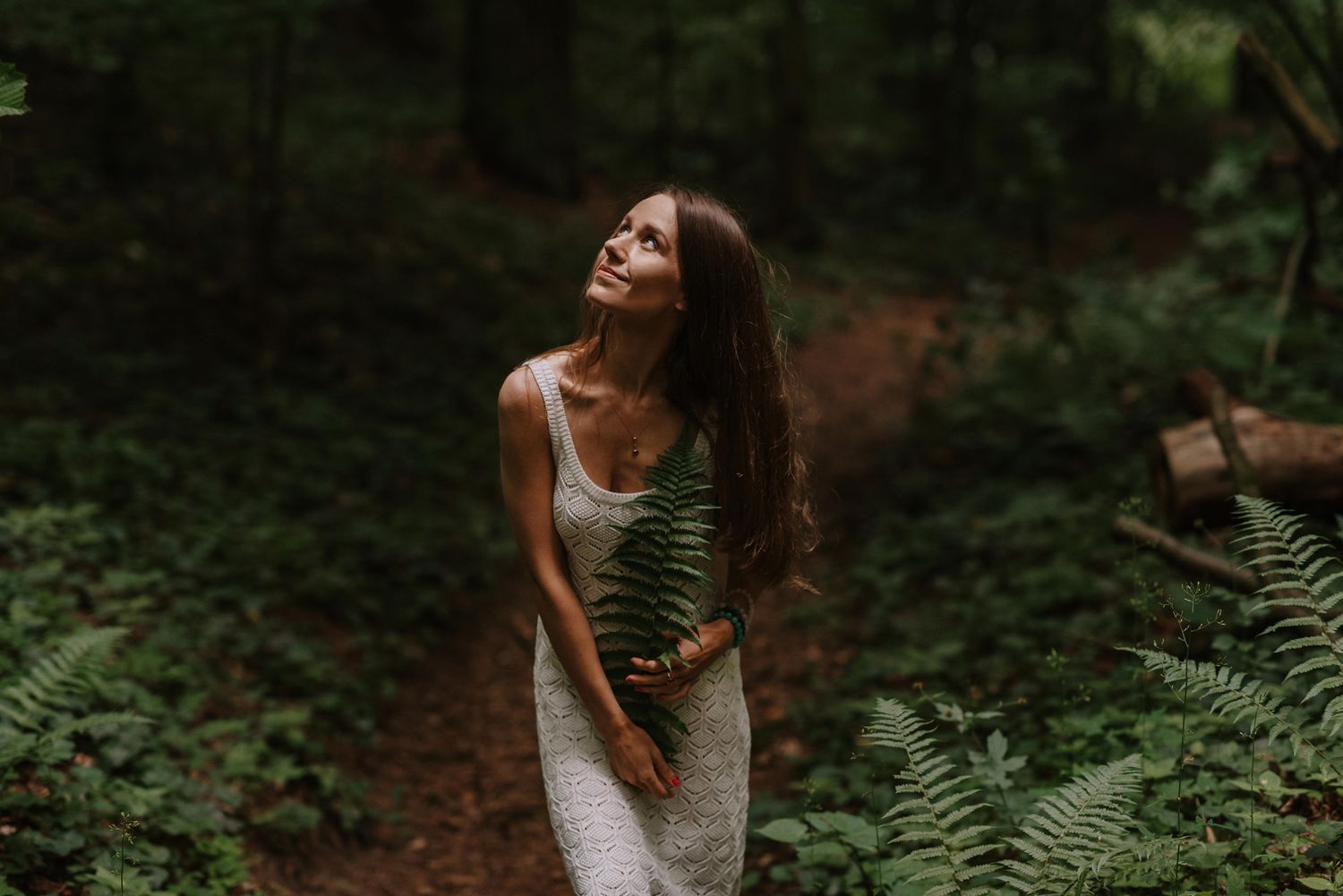 Figure in a white summer dress poses gracefully among ferns and forest vegetation.