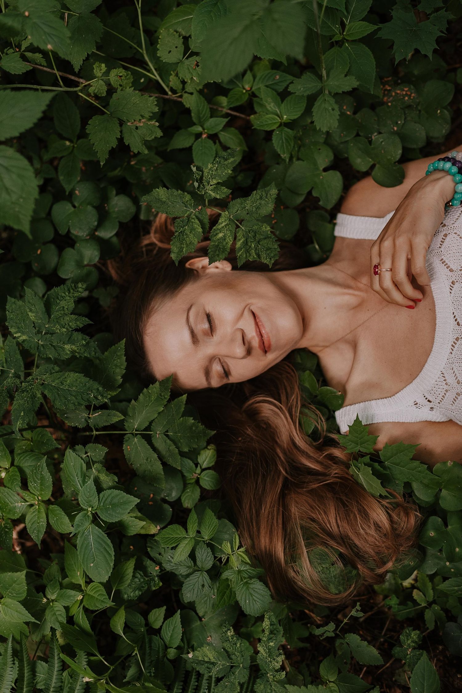 Person lying peacefully among green foliage in a dreamy outdoor portrait setting.