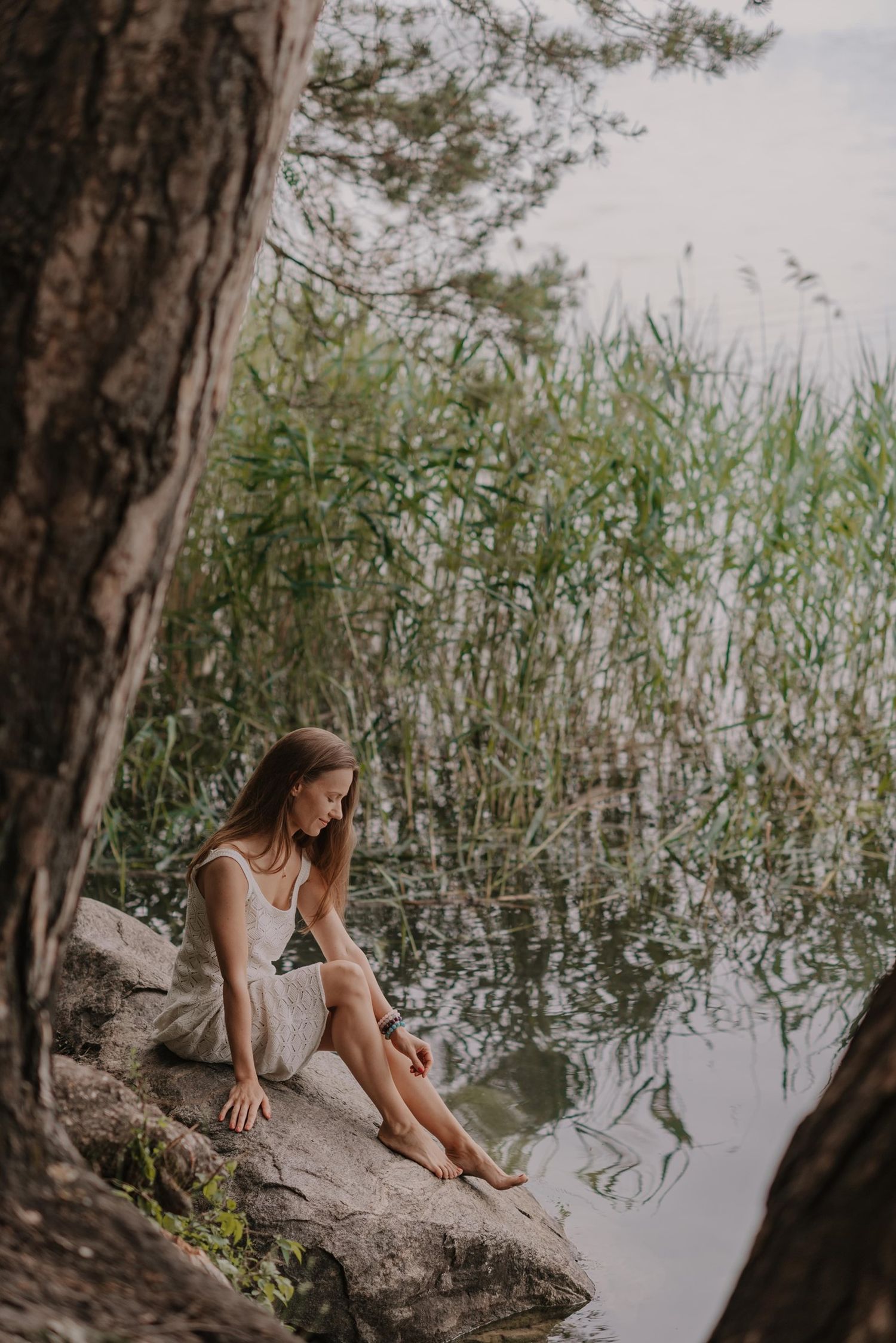 Peaceful waterside scene with someone sitting on rocks near reeds and still water.