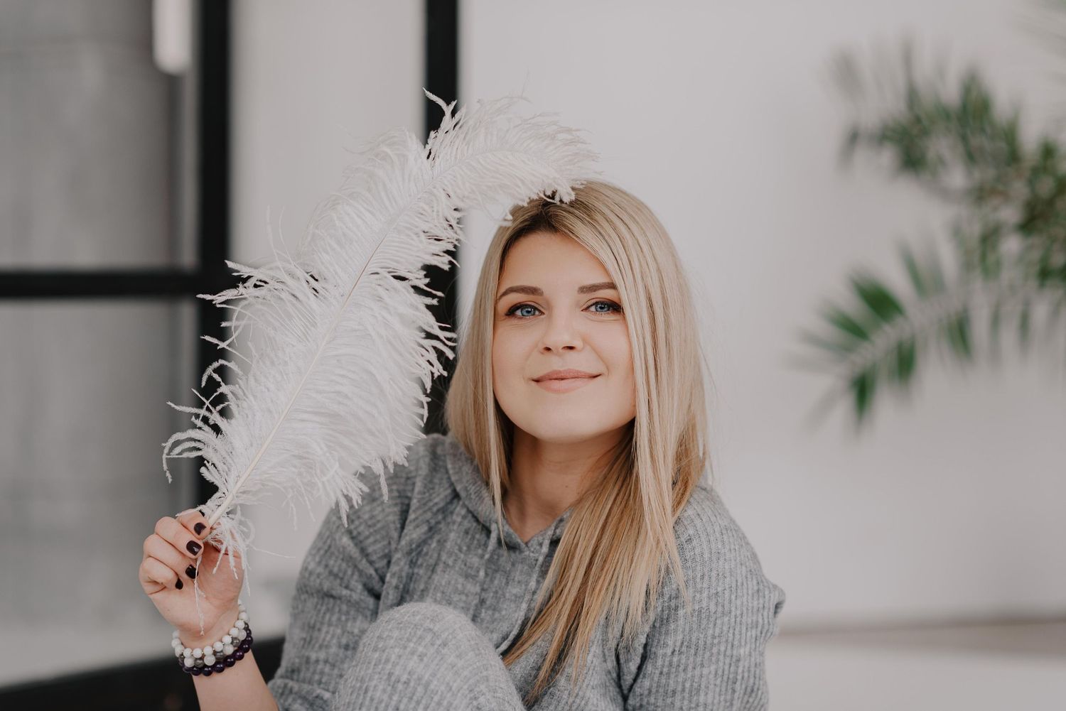 Cozy indoor portrait with soft lighting and feathery decorative elements against white background.