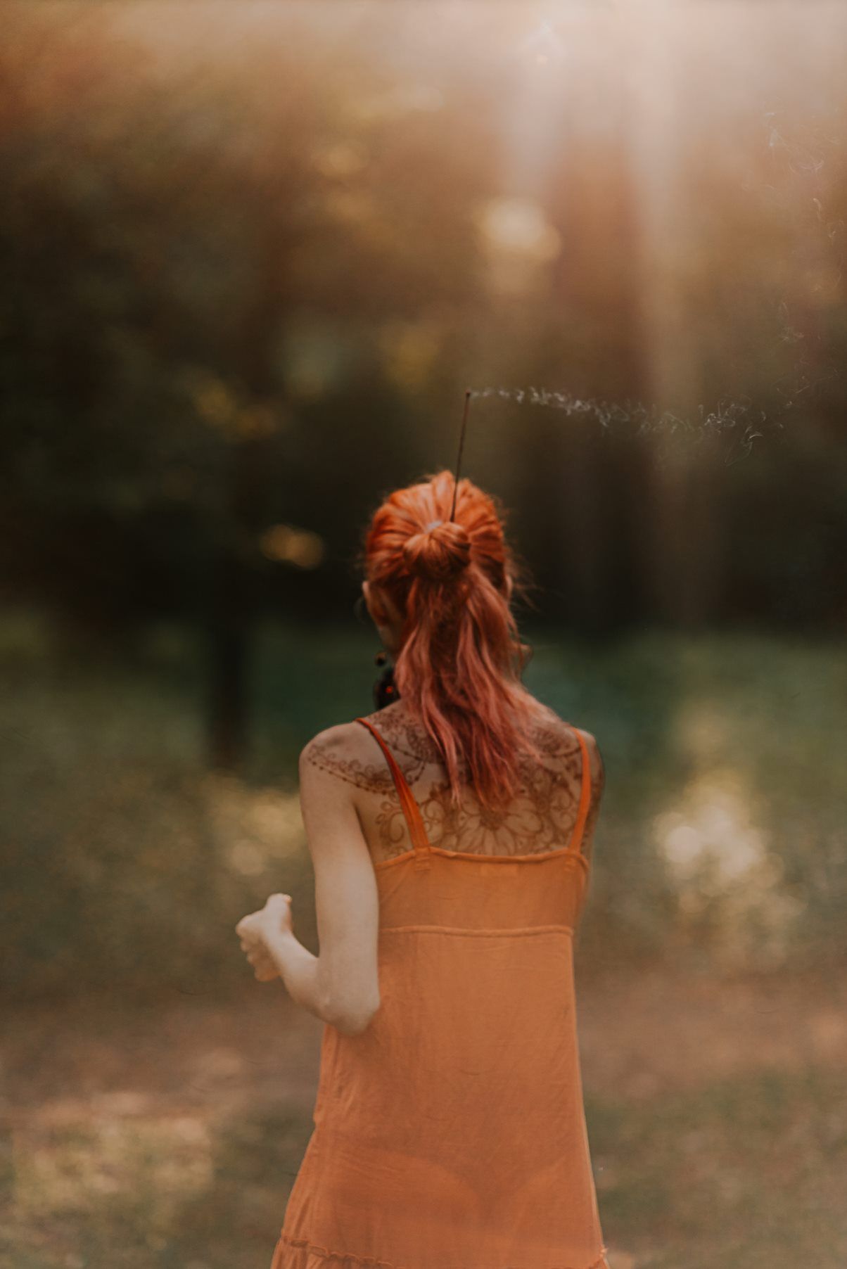 Artistic portrait showing a person in an orange dress against a warm sunlit forest background.