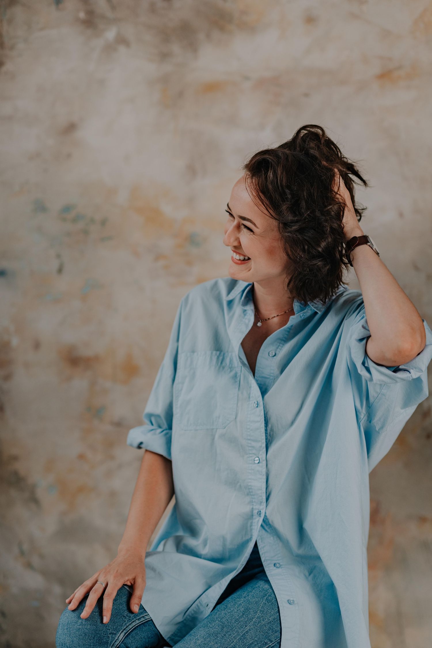 Candid portrait series in light blue shirt against textured wall.