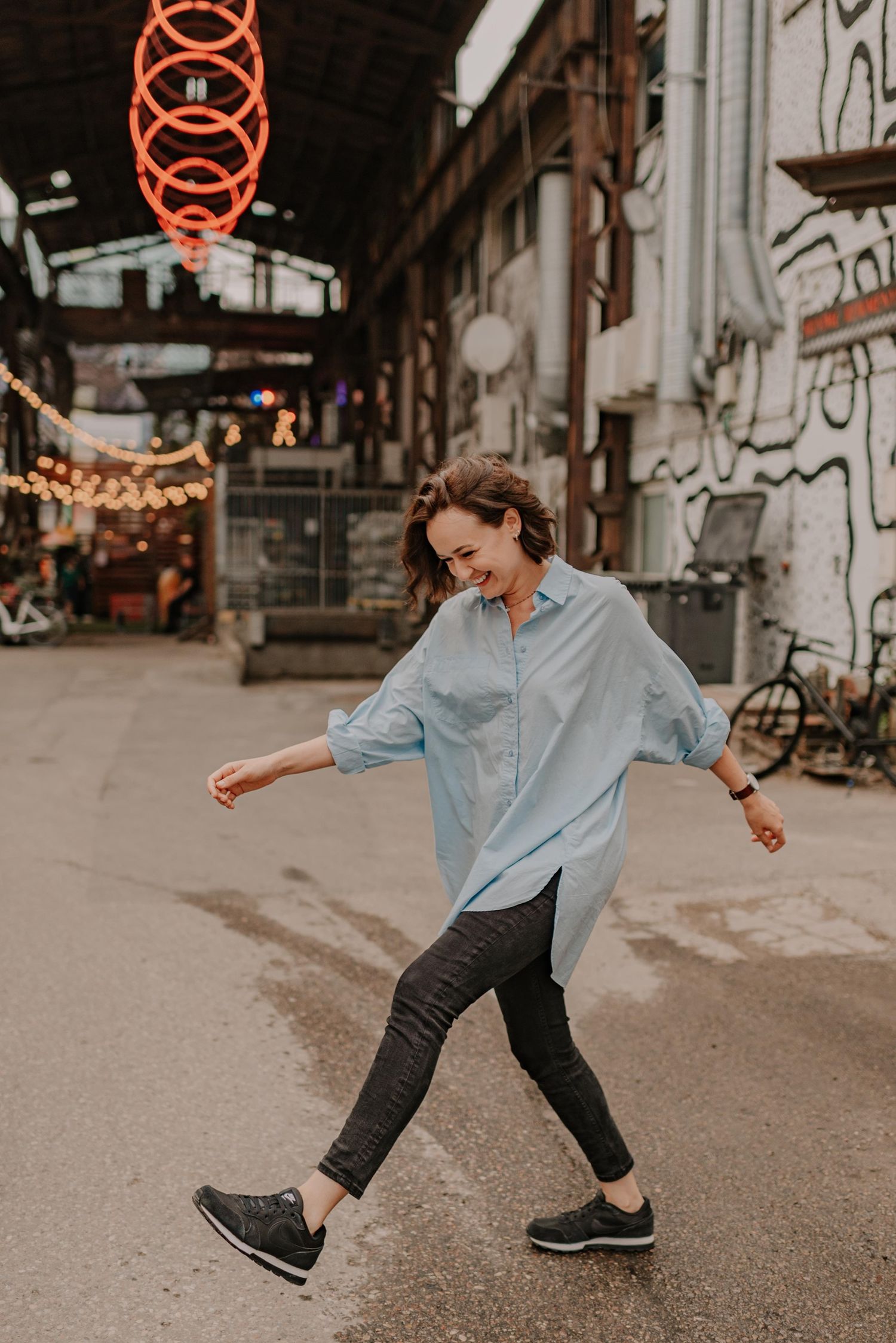 Playful street photography with neon signs and person in casual attire dancing.