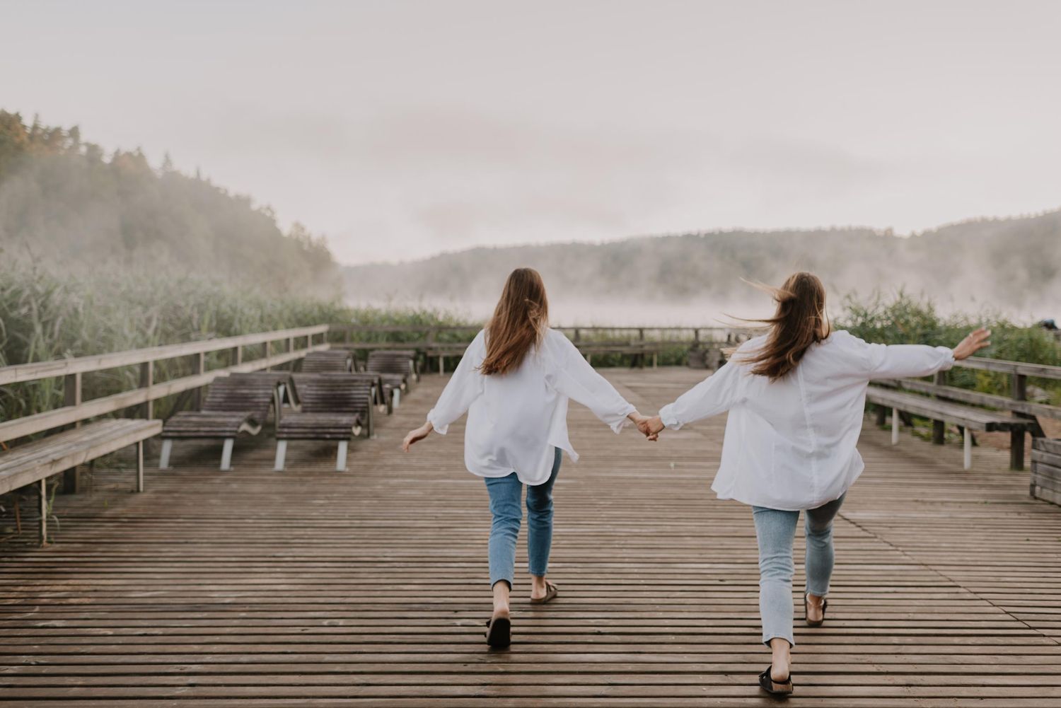 People walking on a wooden boardwalk against a misty mountain backdrop.