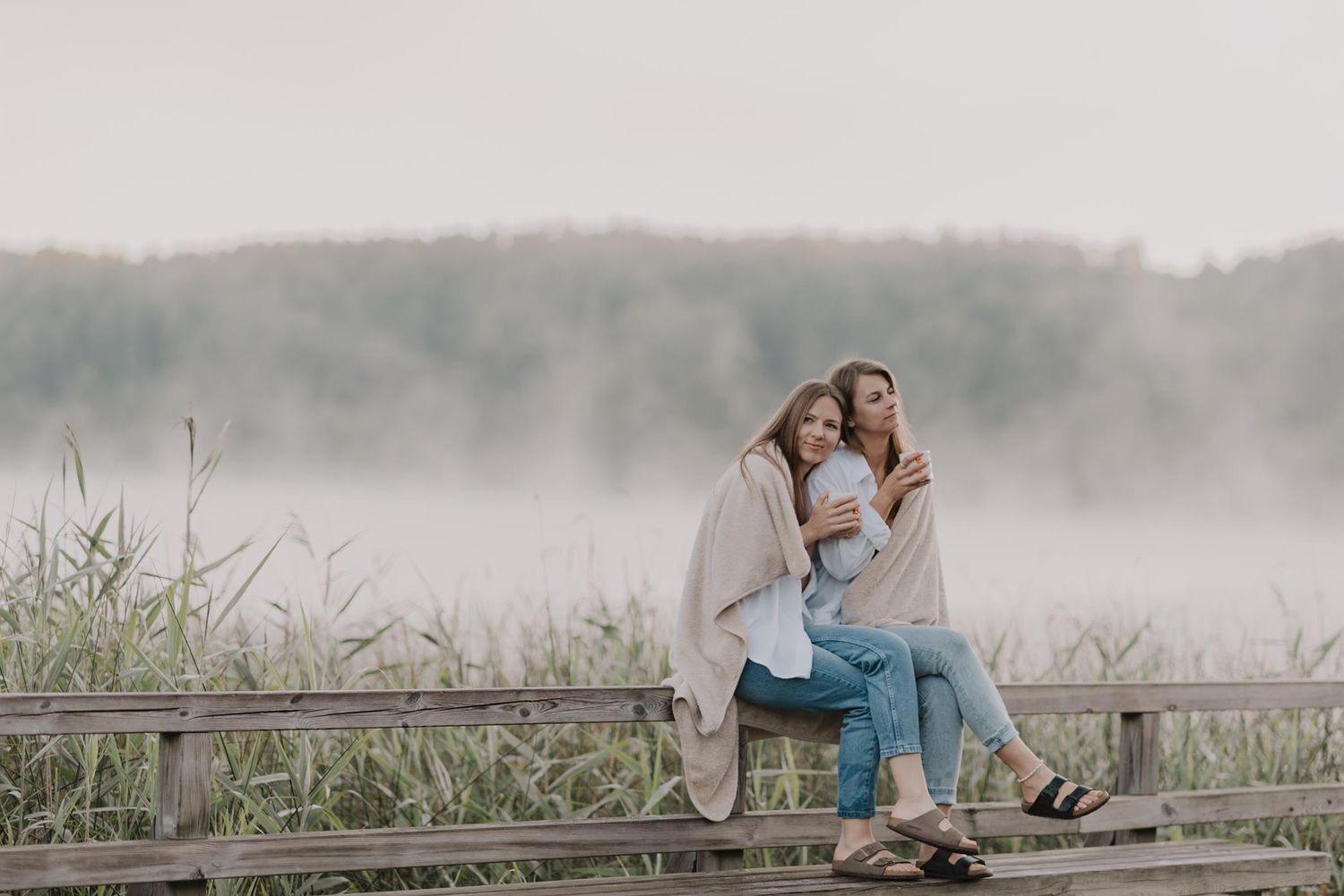 Two people share an intimate moment on a wooden boardwalk surrounded by morning fog.