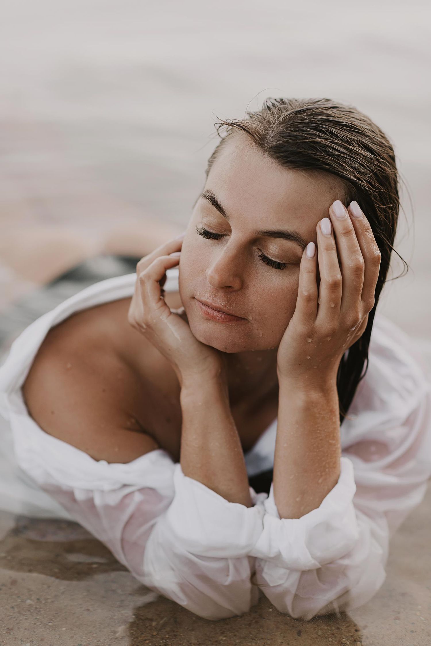 Person in white blouse rests peacefully on beach with eyes closed.