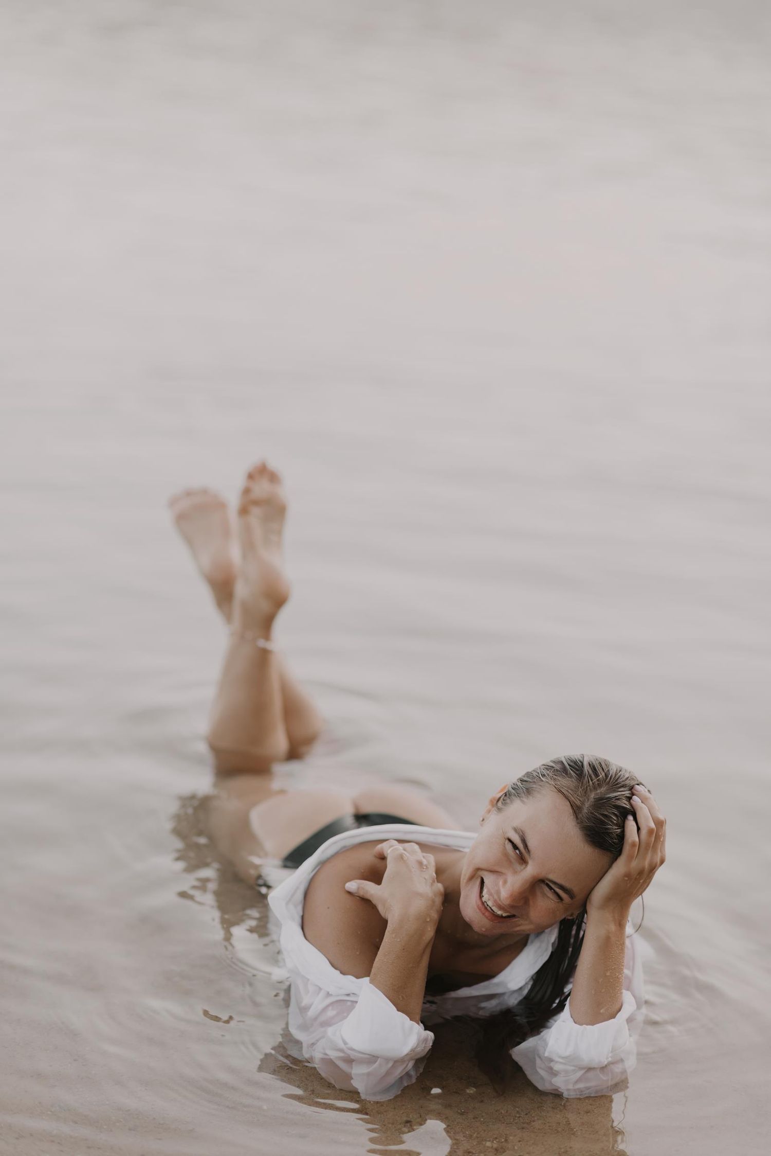 A figure in white fabric lying gracefully in shallow water creating an ethereal and artistic scene.