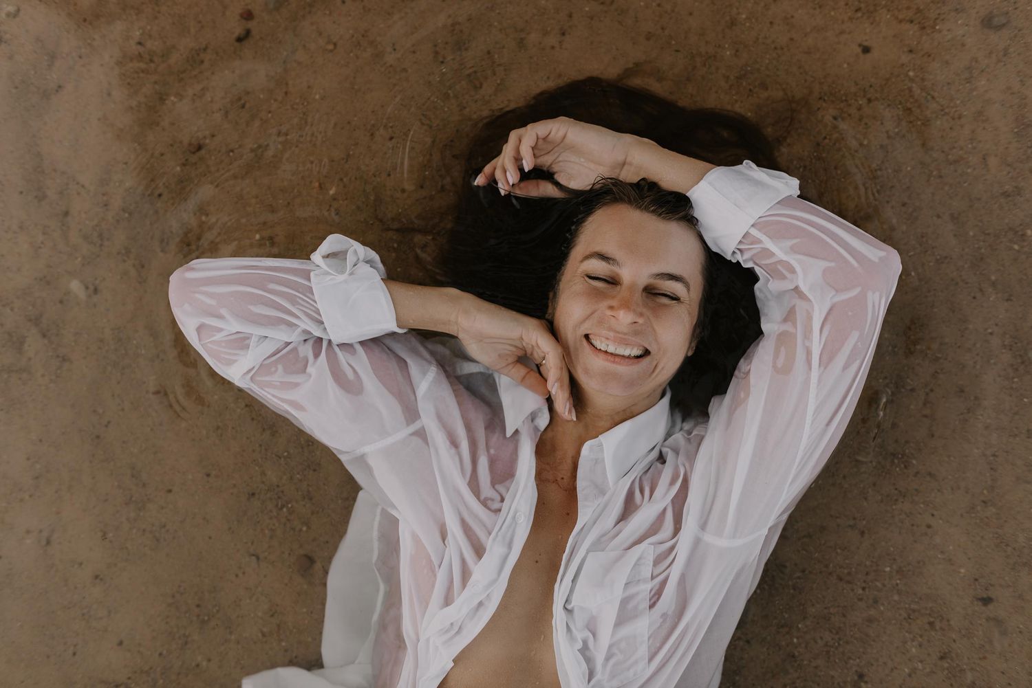 A person in a white shirt lying against a concrete wall with a soft, natural pose.