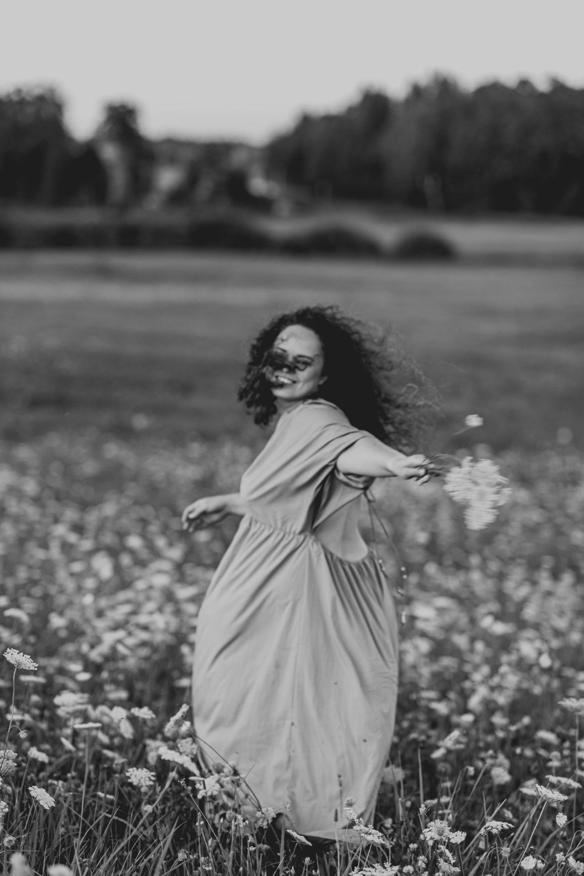 Figure in flowing white dress twirls through a field of wildflowers in black and white.
