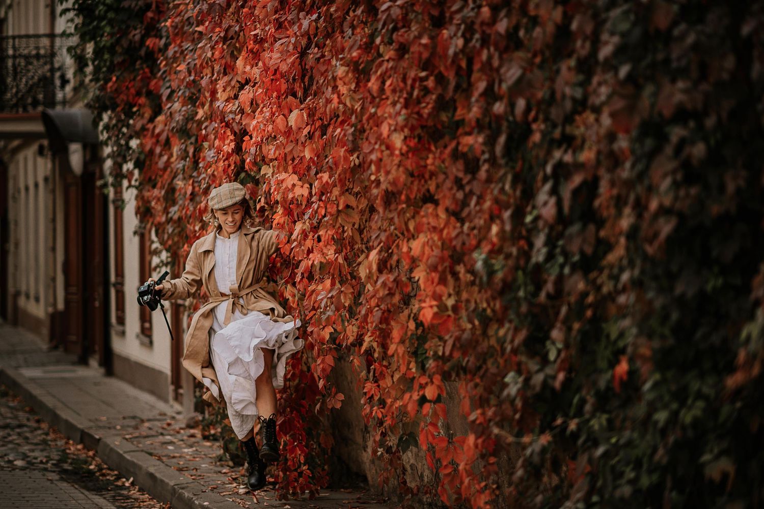 Person walking past wall covered in vibrant red autumn ivy leaves.