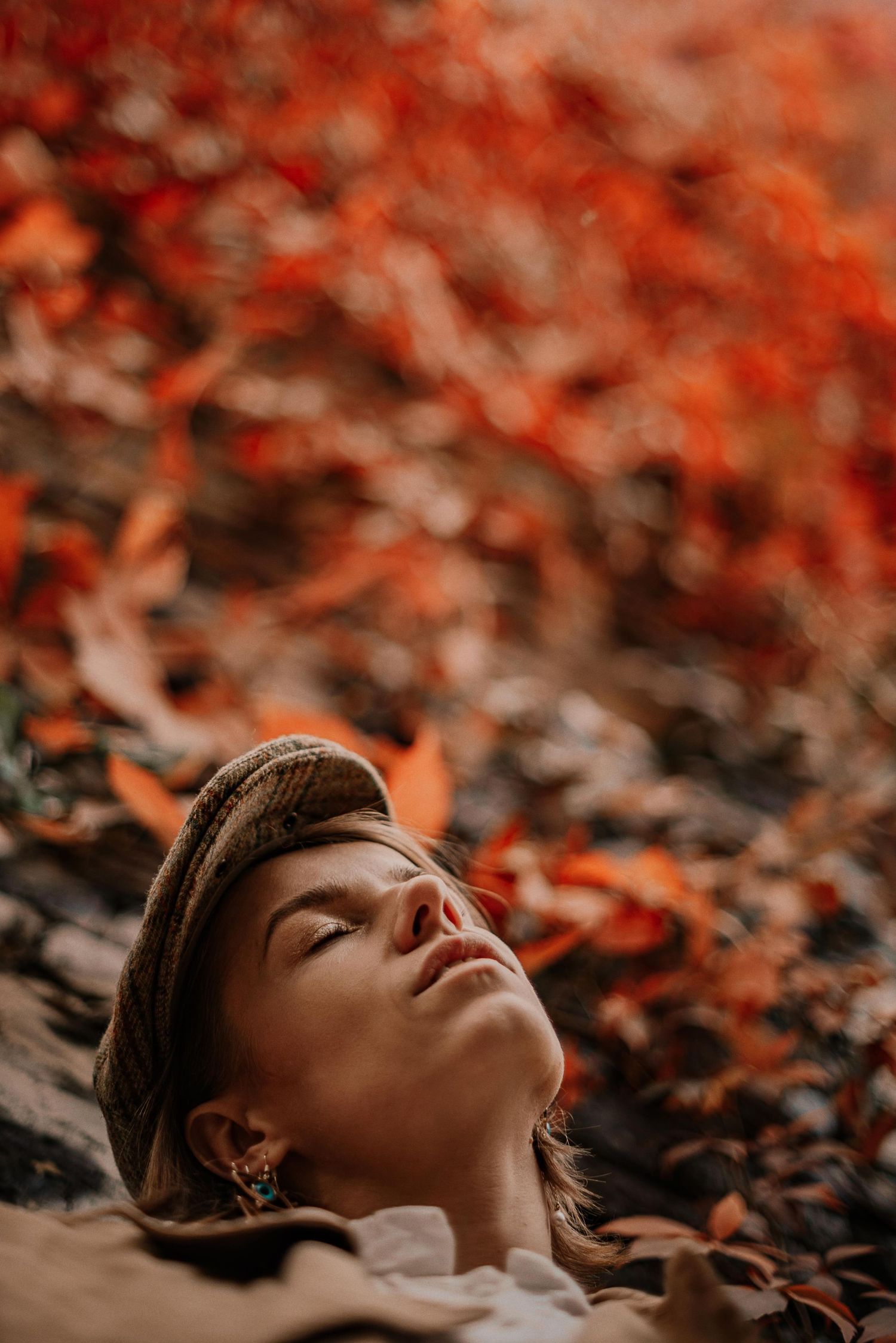 Atmospheric portrait with golden sunlight filtering through vibrant red autumn leaves.