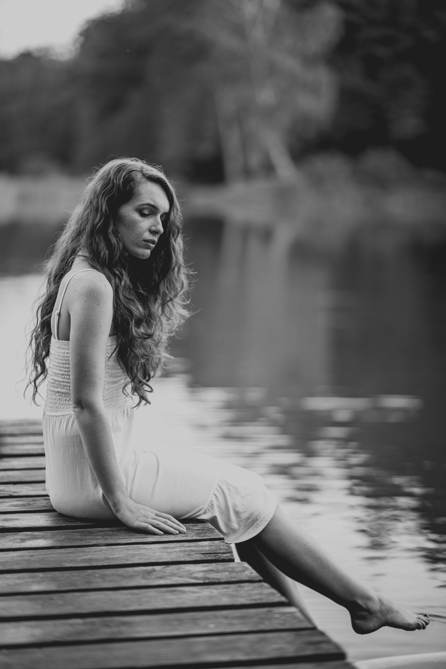 Black and white series of a woman in white dress sitting on wooden dock by tranquil water.