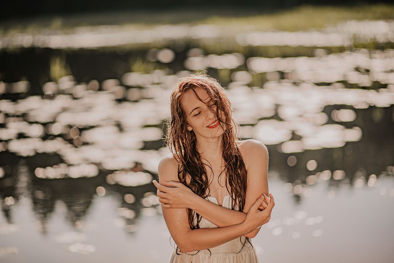 Person with wet hair stands in front of a shimmering lake with scattered light reflections on the water.