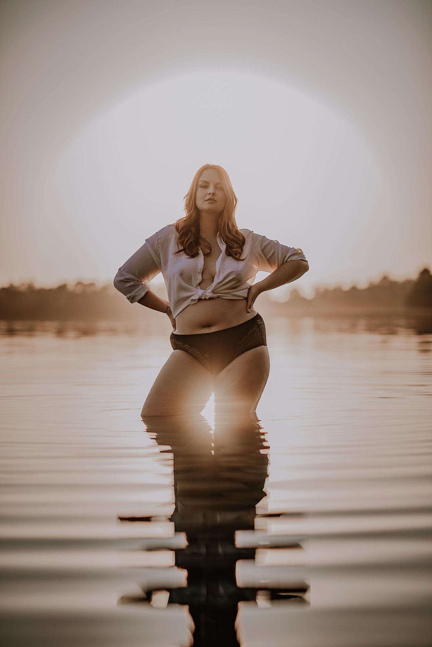 Artistic silhouette of a figure standing in calm water during golden hour.