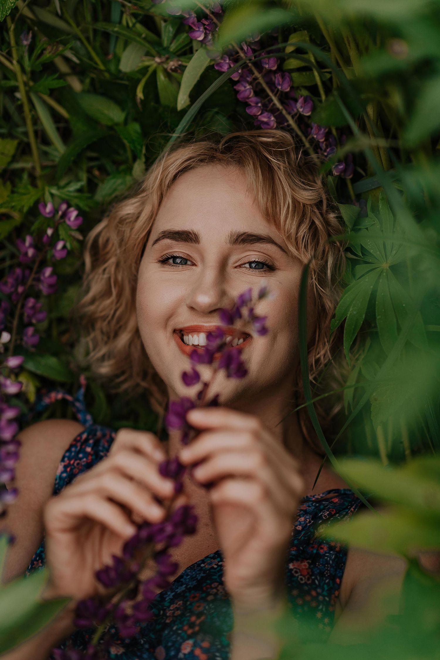 Artistic portrait framed by purple flowers and green foliage in natural lighting.