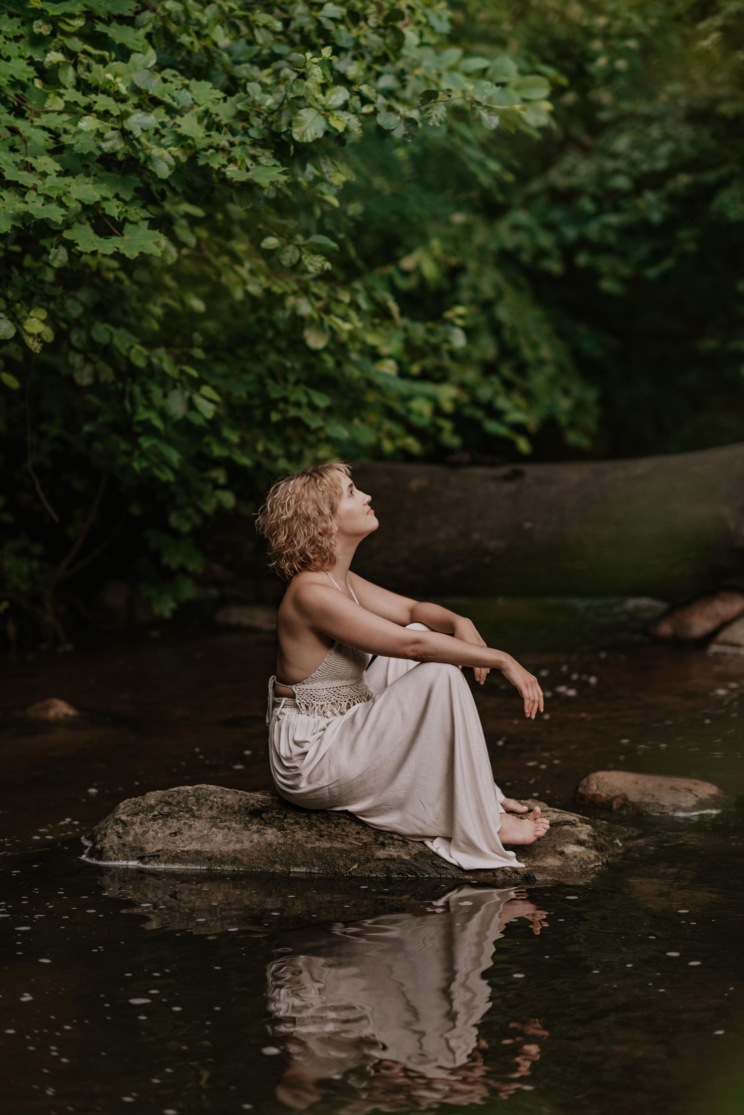 Peaceful scene of someone in white dress sitting on rocks by a serene stream.