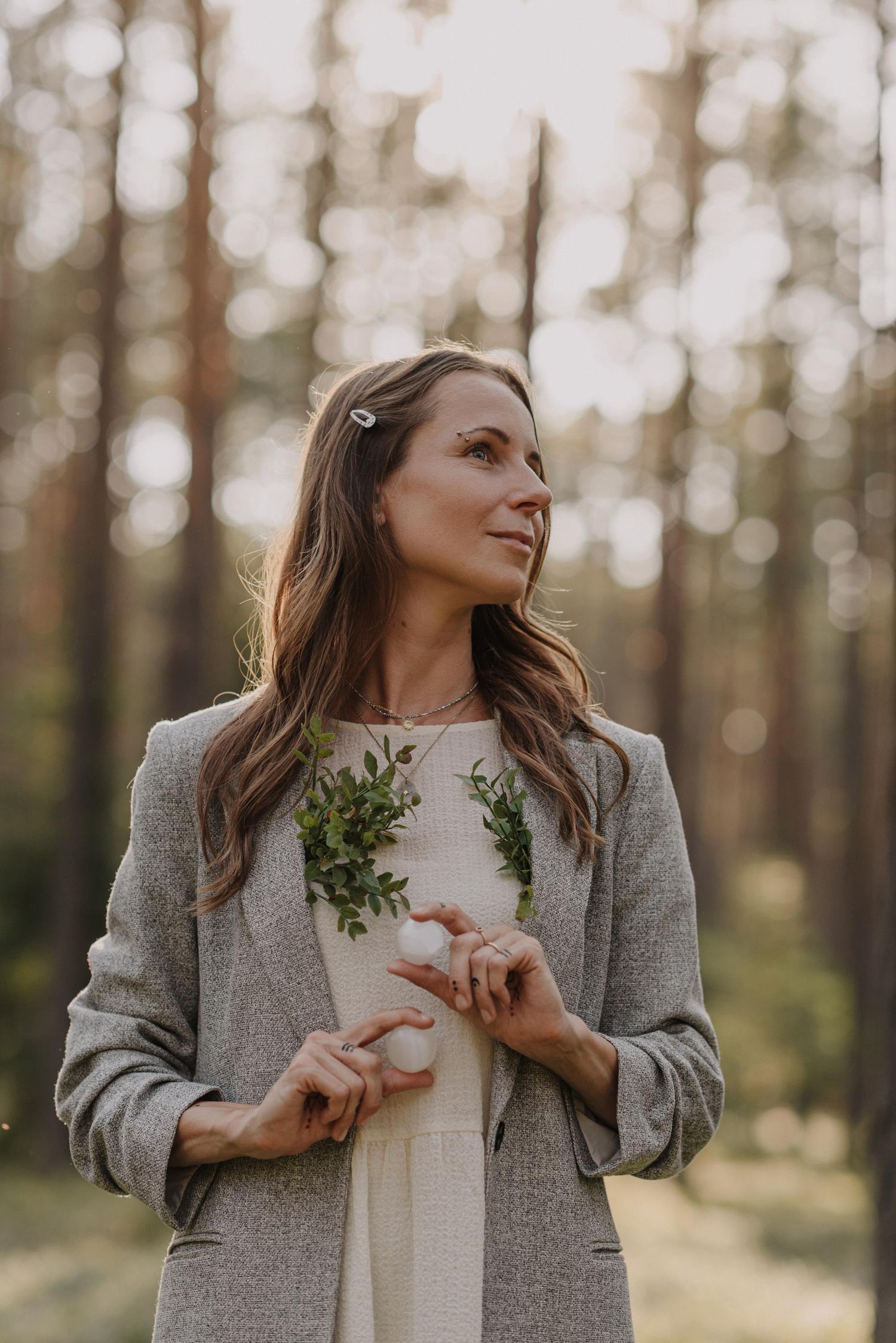 Portrait in a forest wearing a gray blazer with delicate greenery details.