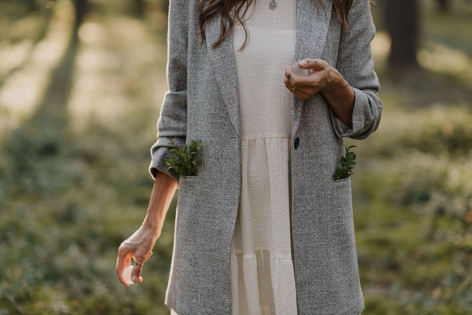 Detail shot of a gray coat and cream dress with natural forest backdrop.