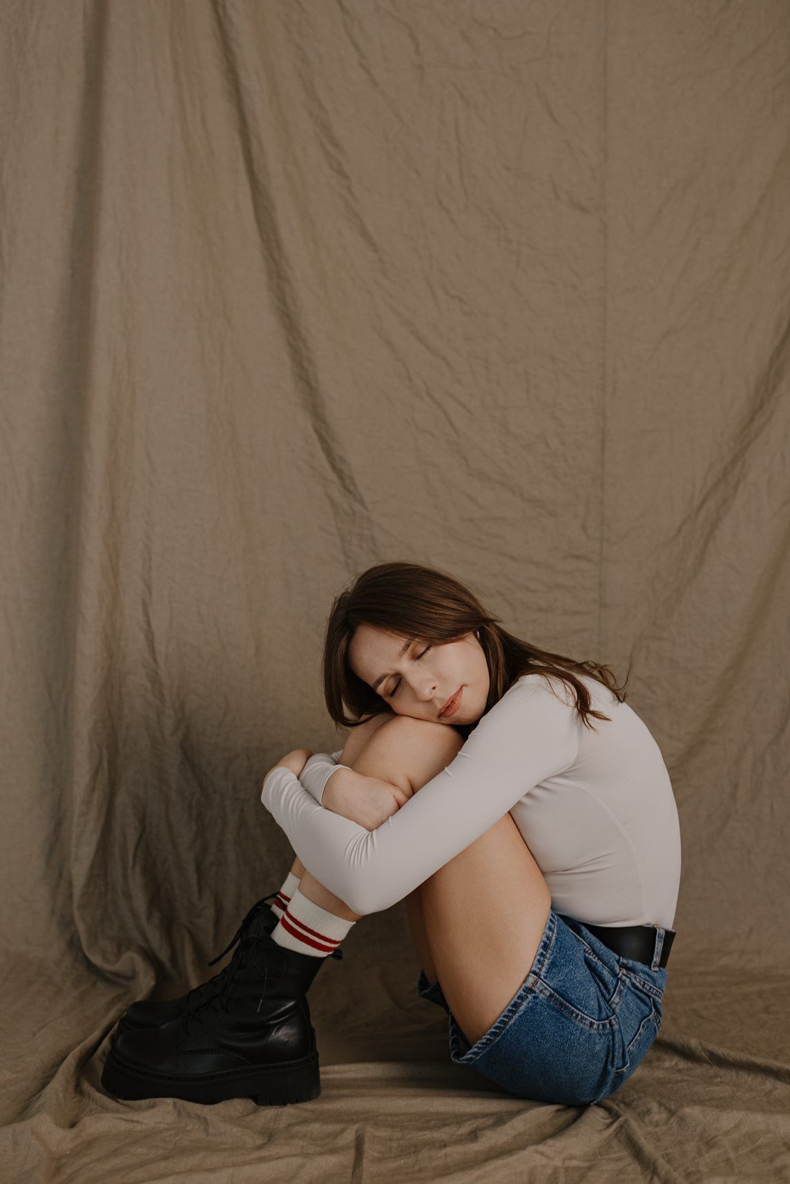 Minimalist portrait in casual wear against neutral fabric backdrop.