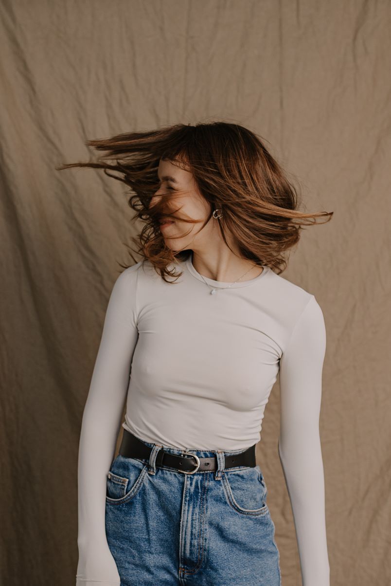 Artistic fashion portrait featuring a white long sleeve top and high waisted blue jeans against a neutral backdrop.