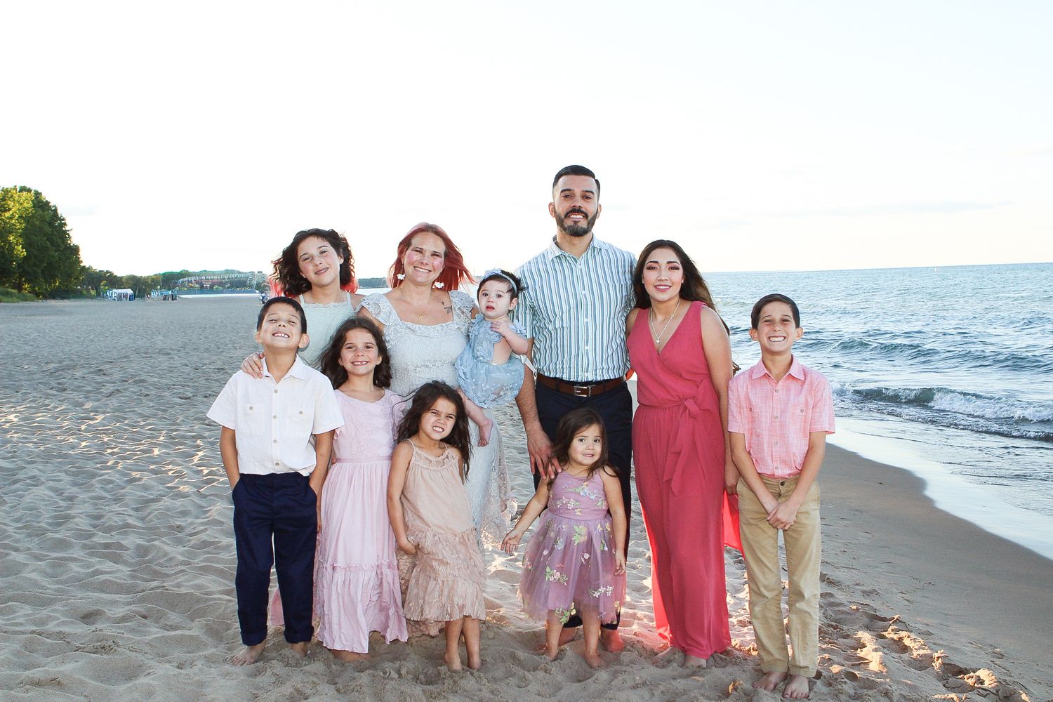 A family poses together on a sandy beach at sunset wearing coordinated outfits in neutral tones.