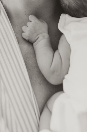 Detail shot of newborn with his arm on mom's chest.