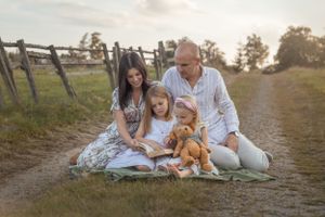 Familjefotografering en sommarkväll. Mamma, pappa och två barn sitter på en filt och läser i en bok.