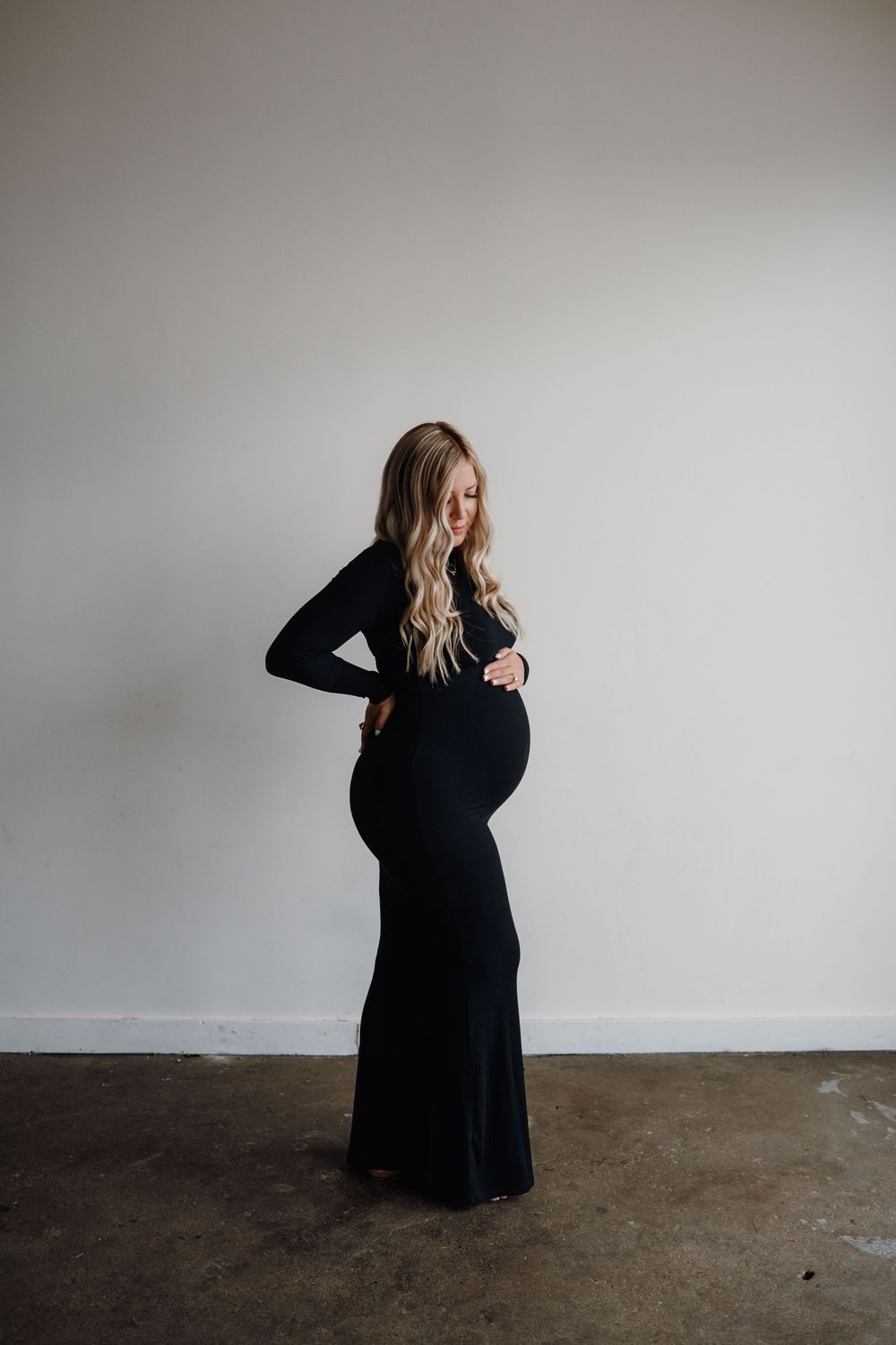 Maternity photoshoot series featuring a woman in black dress against minimal grey background.