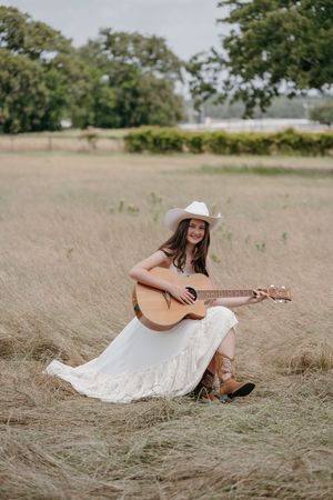 White dress flows in the breeze as acoustic guitar is played in a golden field.