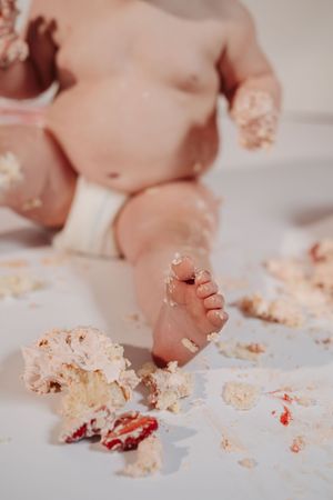 Close-up of tiny baby toes and feet playing with cake crumbs and frosting in a messy smash cake scene.