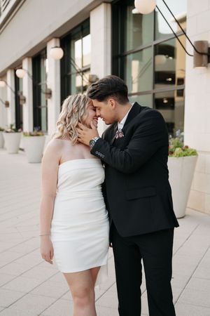 Couple in formal attire shares romantic moments outside modern building with pillars.