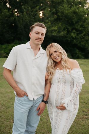 Casual couple's portrait session in white outfits on grassy field.