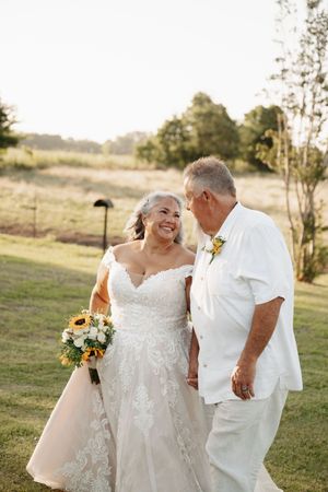 Wedding couple in white attire shares joyful moments together in an outdoor field setting.
