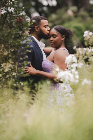 A romantic couple embraces in a garden setting with soft bokeh and delicate flowers in the background.