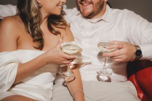 Close up of couple clinking champagne glasses while wearing elegant white attire.