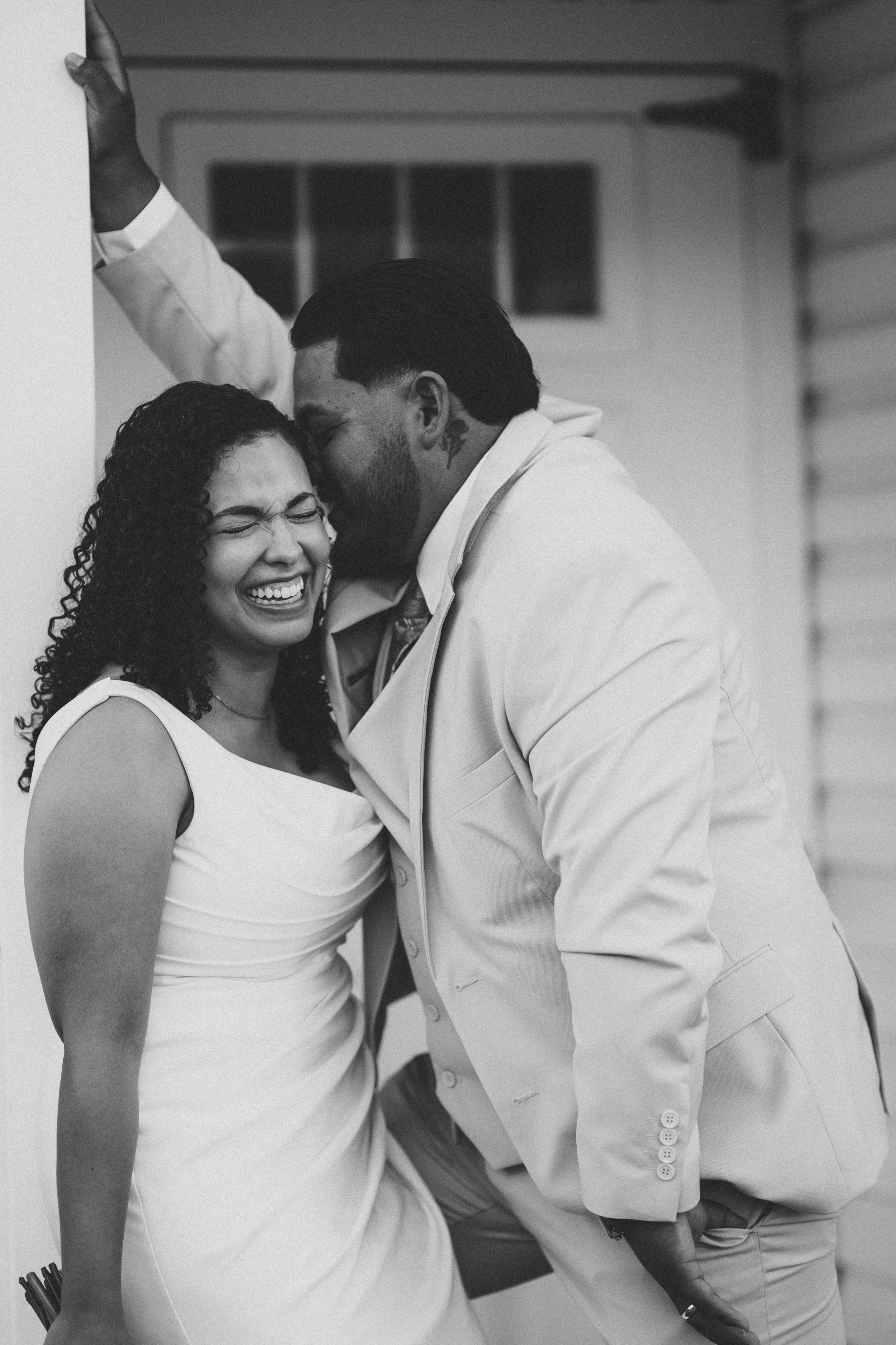 A candid black and white photograph of a joyful couple sharing a loving moment in wedding attire.